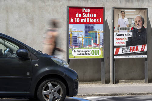 Une personne passe devant les affiches des partis politiques et des associations donnant leurs mots d'ordre pour les votations cantonale et federale du dimanche 14 juin, ce dimanche 7 juin 2026 a Geneve. Les citoyens suisses et genevois voteront sur plusieurs objets federaux: L'initiative populaire "Pas de Suisse a 10 millions !" La modification de la loi federale sur le service civil. Deux objet en votations cantonale: La loi constitutionnelle modifiant la constitution de la Republique et canton de Geneve"Pour une expression non ostentatoire des conviction religieuses". La loi modifiant la loi sur "Les heures d'ouverture des magasins ouverture du dimanche" (KEYSTONE/Martial Trezzini)
